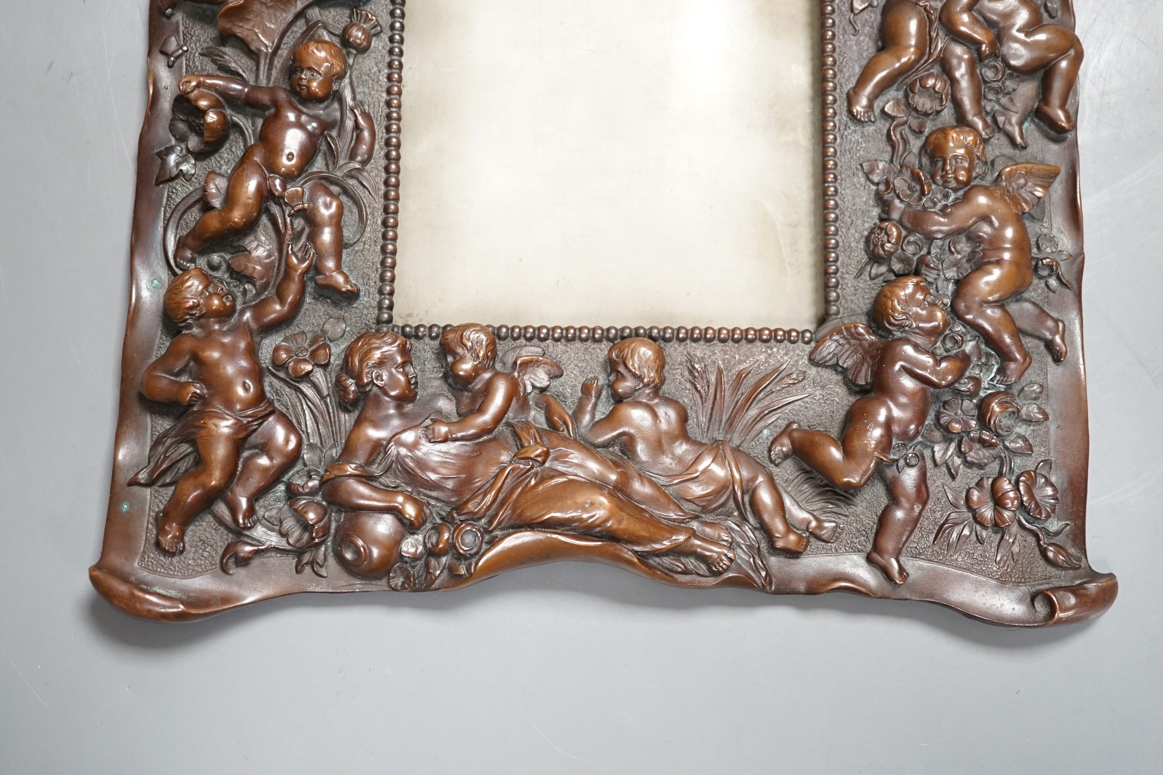 A bronzed copper frame decorated with putti, circa 1900. 28.5cm long